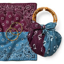A handbag made from a folded bandana fabric with a bamboo-style handle, shown alongside a matching bandana cloth and two round metallic rings on a white background.